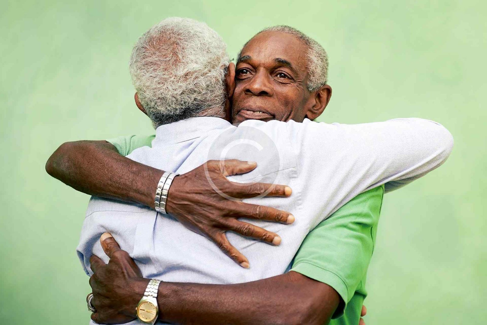 صورة مخزون محمية بحقوق النشر لرجلين مسنّين يتعانقان بحرارة على خلفية خضراء | Copyright-watermarked stock photo of two elderly men warmly embracing against a green background
