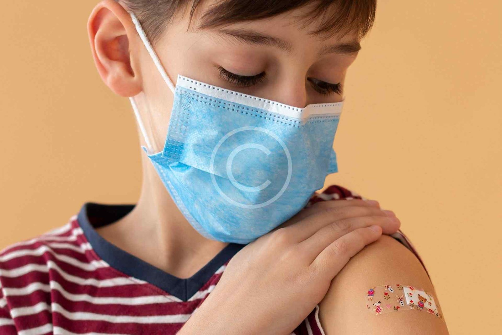 صورة مخزون محمية بحقوق النشر لصبي يرتدي كمامة زرقاء وعلى ذراعه لصقة طبية ملونة | Copyright-watermarked stock photo of a boy wearing a blue mask with a colorful bandage on his arm
