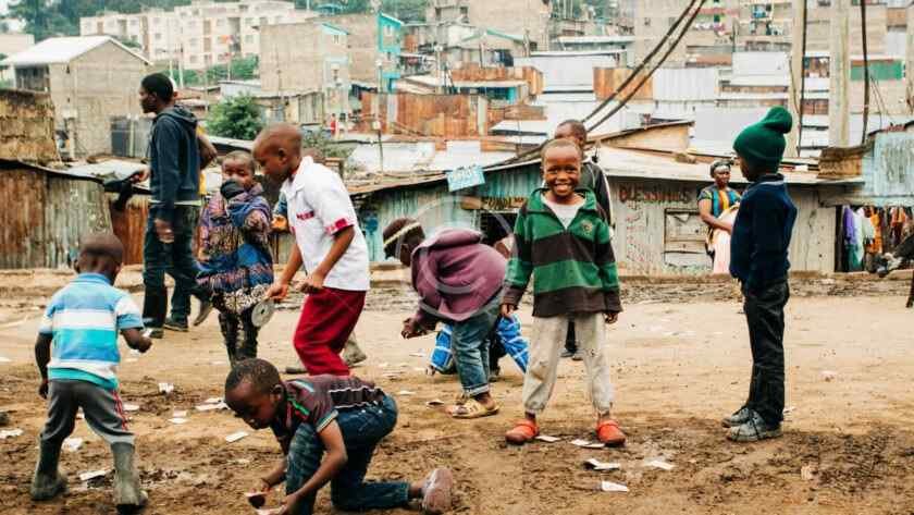 صورة مخزنة محمية بحقوق نشر لمجموعة أطفال يلعبون في حي عشوائي متواضع | Copyright-watermarked stock photo of a group of children playing in a modest informal settlement street