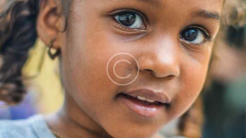 صورة مخزنة محمية بحقوق نشر لوجه طفلة ترتدي قرطاً بعدسة مقربة | Copyright-watermarked stock close-up of a child's face wearing an earring