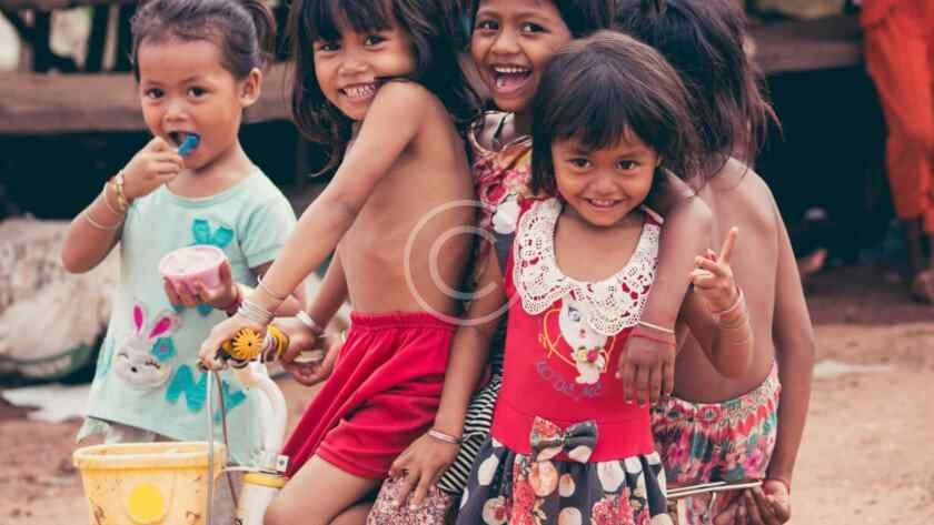 صورة مخزنة محمية بحقوق نشر لمجموعة أطفال مبتسمين يتشاركون دراجة في قرية | Copyright-watermarked stock photo of a group of smiling children sharing a bicycle in a village setting