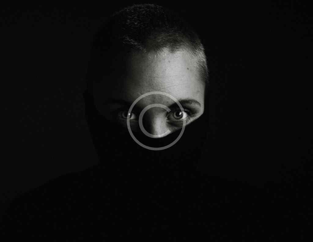 صورة مخزنة محمية بحقوق نشر لوجه شخص في الظل مع إضاءة خافتة على العينين فقط | Copyright-watermarked stock photo of a shadowed face with only the eyes faintly lit