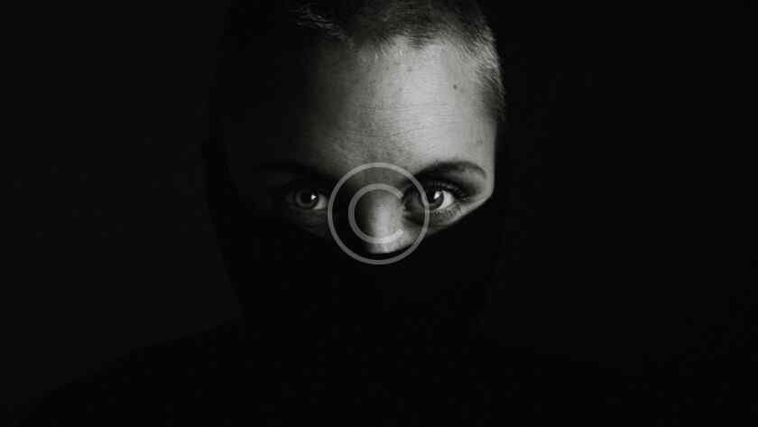 صورة مخزنة محمية بحقوق نشر لوجه شخص في الظل مع إضاءة خافتة على العينين فقط | Copyright-watermarked stock photo of a shadowed face with only the eyes faintly lit