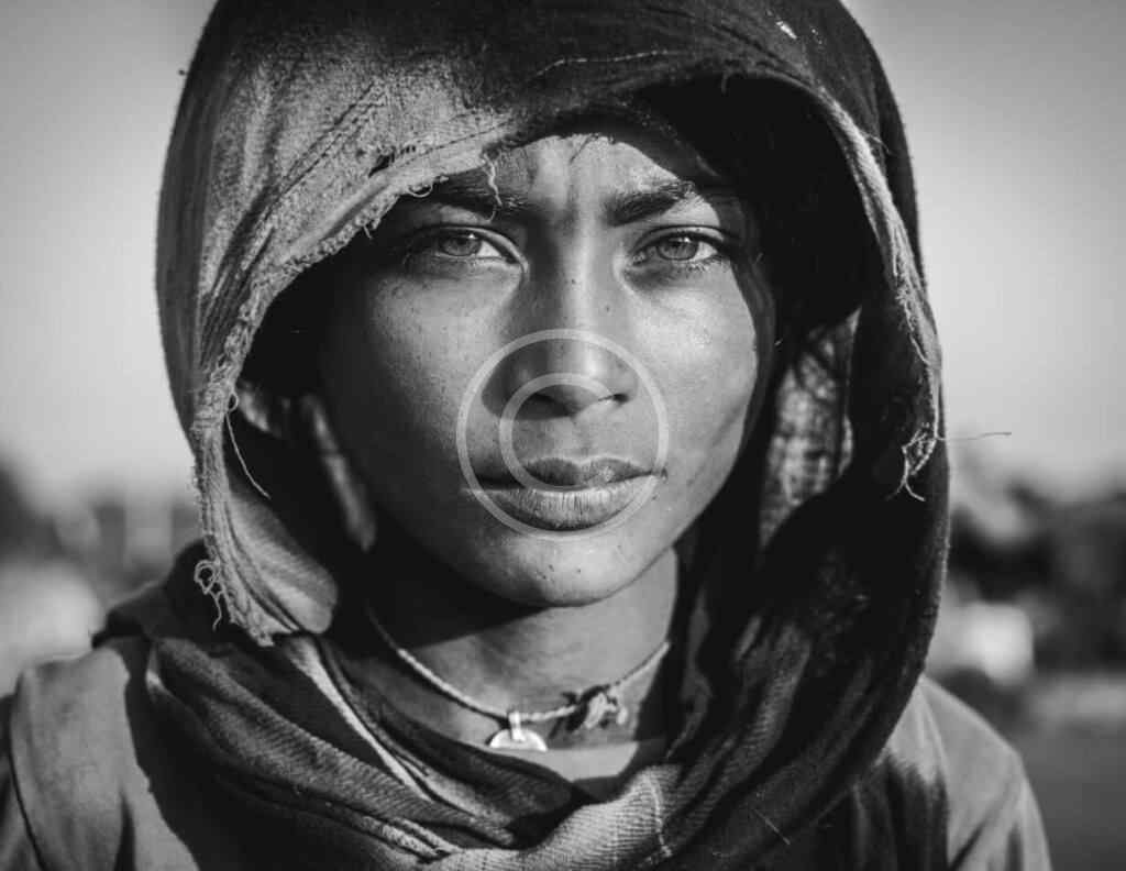 صورة مخزنة محمية بحقوق نشر لوجه شخص مغطى بوشاح بالٍ بالأبيض والأسود | Copyright-watermarked black-and-white stock close-up of a face wrapped in a worn hooded scarf