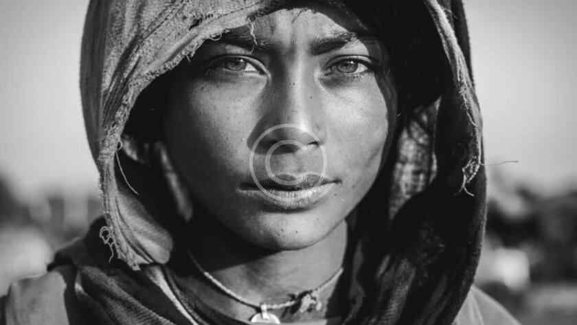 صورة مخزنة محمية بحقوق نشر لوجه شخص مغطى بوشاح بالٍ بالأبيض والأسود | Copyright-watermarked black-and-white stock close-up of a face wrapped in a worn hooded scarf