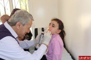 طبيب يفحص حنجرة طفلة باستخدام منظار طبي داخل غرفة معاينة بيضاء | A doctor examines a girl throat with a medical scope inside a white examination room