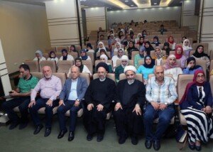 صفوف من الممرضات والمسؤولين ورجل دين يجلسون في قاعة محاضرات مدرجة | Rows of nurses, officials and a cleric sit in a tiered lecture hall