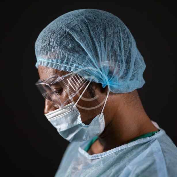 صورة مخزون محمية بحقوق النشر لشخص يرتدي غطاء رأس طبي ونظارات واقية وكمامة | Copyright-watermarked stock photo of a person wearing a surgical cap, goggles, and a face mask