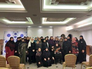 سيدات يقفن معاً لصورة جماعية أمام خلفية بيضاء مزخرفة بأشكال هندسية زرقاء | Women stand together for a group photo in front of a white backdrop decorated with blue geometric shapes