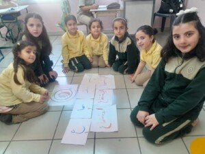 سبع تلميذات يجلسن على الأرض حول بطاقات ملوّنة مكتوب عليها حروف عربية | Seven pupils sit on the floor around colorful cards with Arabic letters