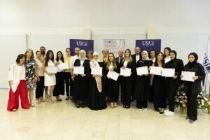 مجموعة كبيرة من الأشخاص يحملون شهادات ويقفون أمام لافتات جامعة القديس يوسف وشراكة دان مشن | A large group of people holding certificates standing before Université Saint-Joseph and Danmission banners