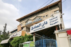 واجهة مبنى دار الصادق للتربية والتعليم التابع لجمعية المبرّات الخيرية مع لافتة كبيرة وبوابة زرقاء | The facade of the Dar Al-Sadeq education building of the Al-Mabarrat Charitable Association with a large sign and a blue gate