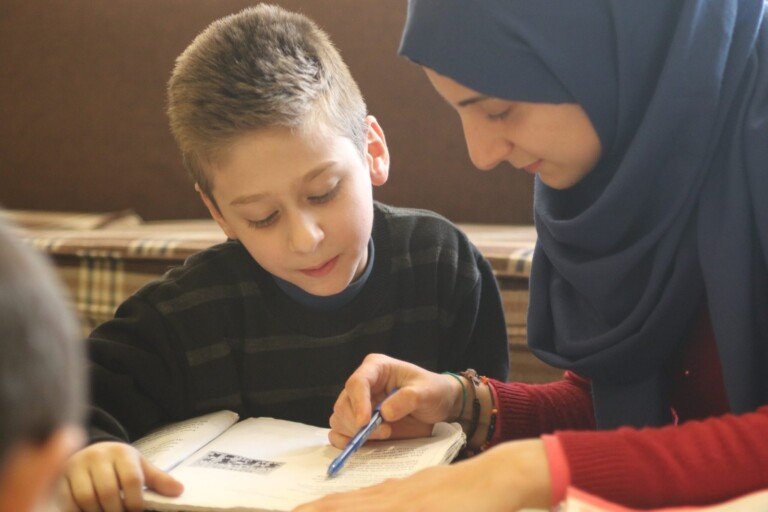 معلمة تساعد طالبًا في حل واجب دراسي داخل صف في مبرّة الإمام الخوئي في لبنان | Teacher assisting a student with schoolwork inside a classroom at Imam Al-Khoei Care Institution in Lebanon
