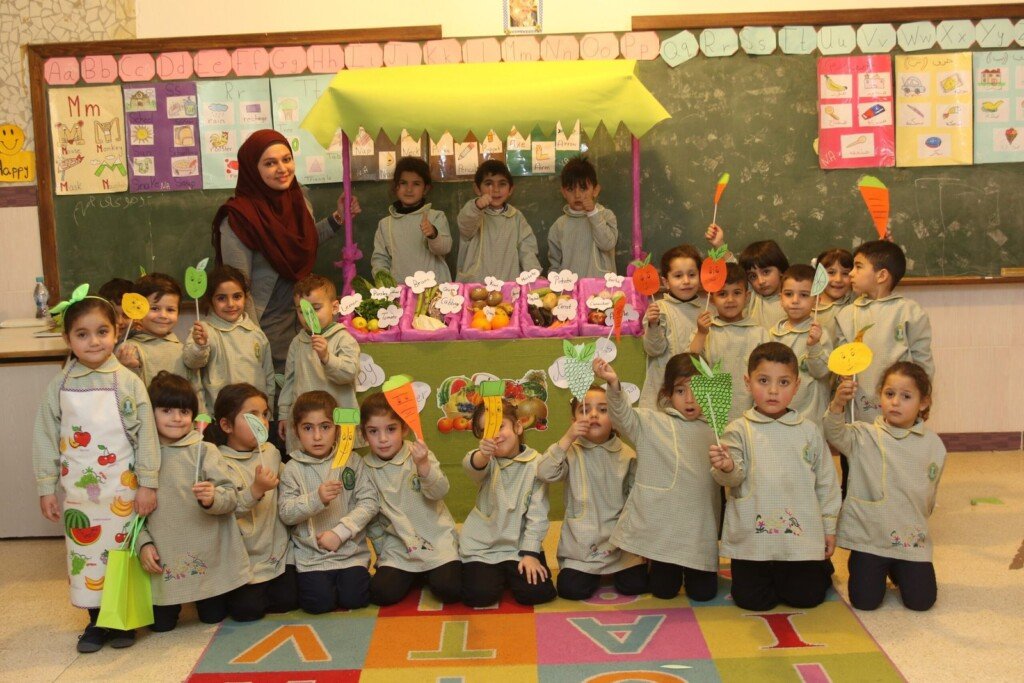 طلاب في صف مدرسي يشاركون في نشاط تعليمي تفاعلي مع مجسمات وخضار وفواكه ورقية | Students in a classroom participating in an interactive educational activity with handmade fruit and vegetable models