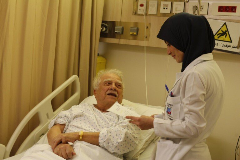 ممرضة تطمئن على مريض مسن في غرفته بمستشفى بهمن | A nurse checking on an elderly patient in his room at Bahman Hospital