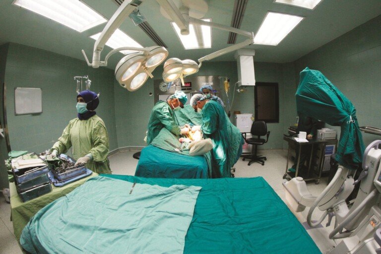 فريق طبي يجري عملية جراحية تحت أضواء الجراحة في غرفة عمليات مجهزة بمستشفى بهمن | A medical team performing surgery under operating lights in a fully equipped operating room at Bahman Hospital