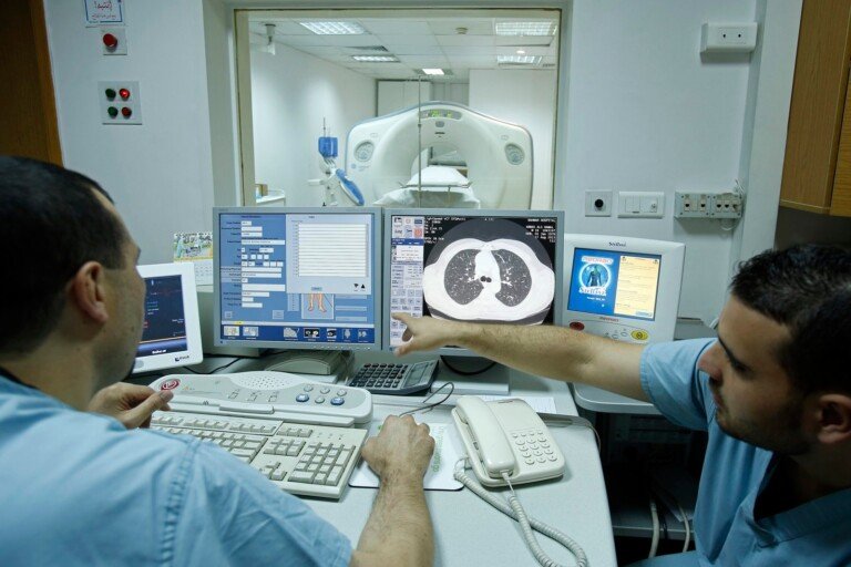 تقنيان يتابعان صور التصوير الطبقي المحوري في قسم الأشعة بمستشفى بهمن | Two technicians reviewing CT scan images in the radiology department at Bahman Hospital