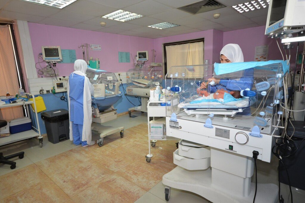 ممرضتان تعتنيان بحديثي الولادة داخل الحاضنات في العناية الفائقة بمستشفى بهمن | Two nurses caring for newborns in incubators at Bahman Hospital's NICU