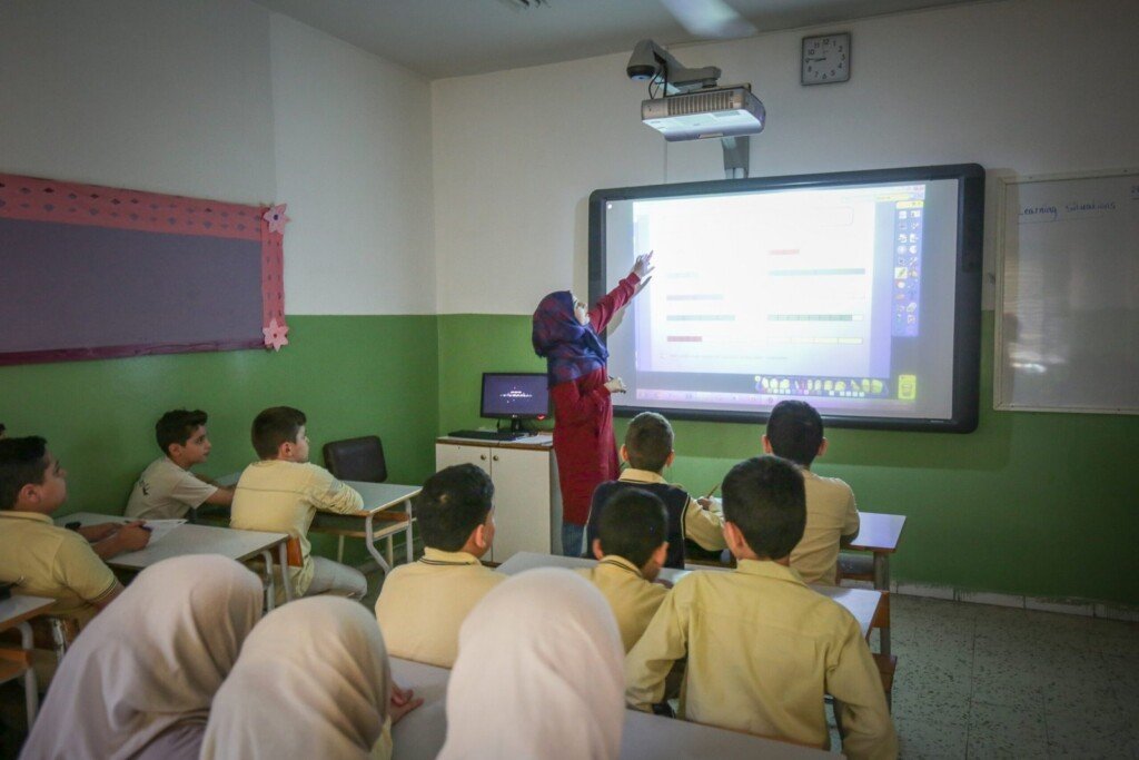 معلمة تشرح درساً باستخدام شاشة ذكية تفاعلية أمام الطلاب داخل صف مدرسي | Teacher explaining a lesson using an interactive smart board in front of students inside a classroom
