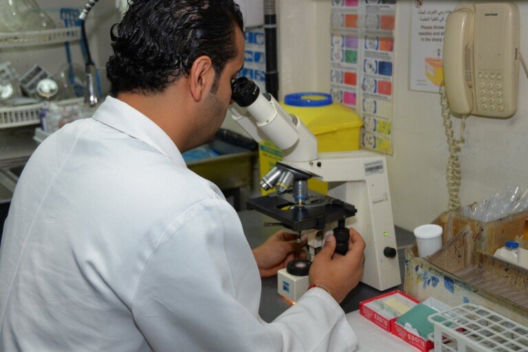 فني مختبر يفحص عينة تحت المجهر في مختبر مستشفى بهمن | A lab technician examining a sample under the microscope at Bahman Hospital laboratory