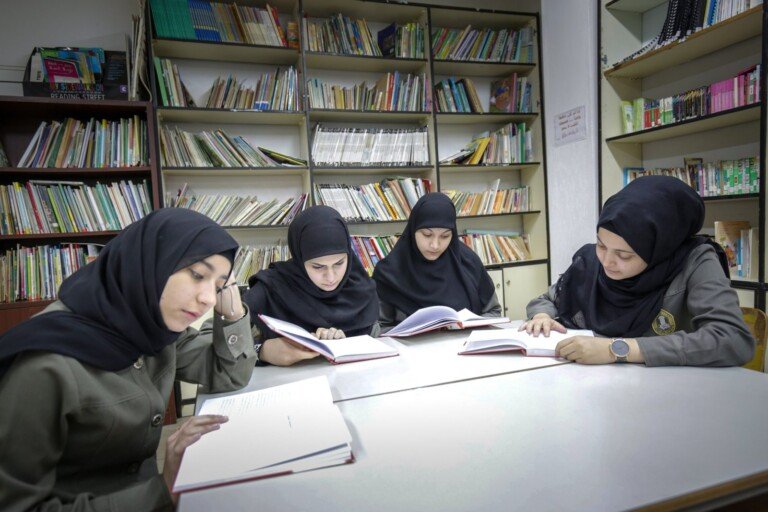 أربع طالبات يقرأن كتباً حول طاولة مكتبة دار الصادق | Four students reading books around a library table at Dar Al-Sadiq