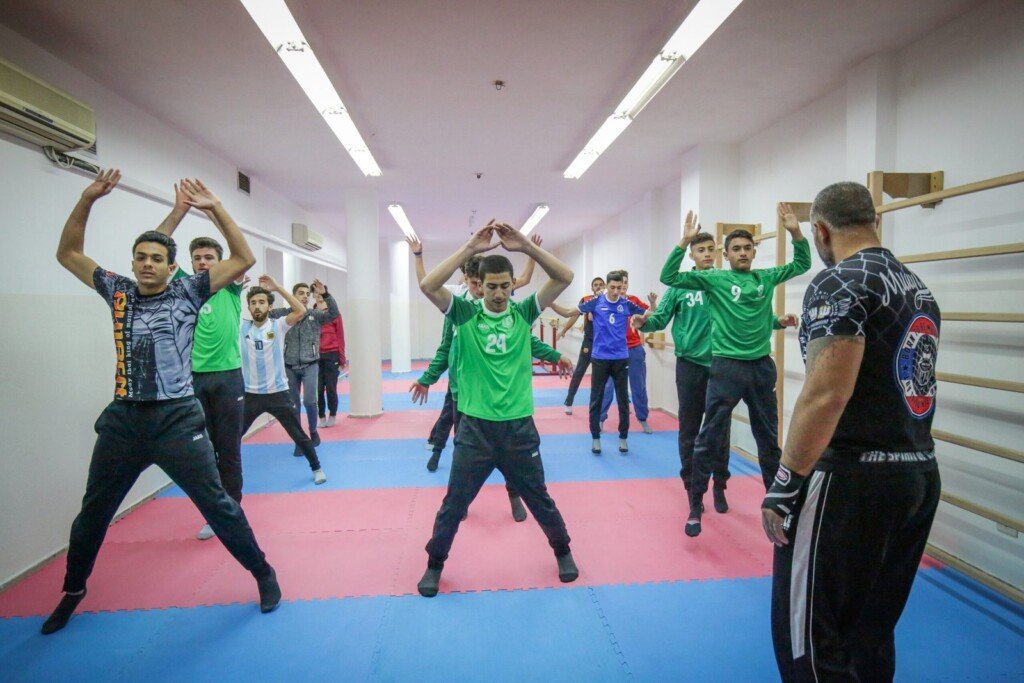 طلاب يؤدون تمارين الإحماء في القاعة الرياضية بدار الصادق بإشراف مدرب | Students doing warm-up drills in the Dar Al-Sadiq sports hall under a coach's supervision