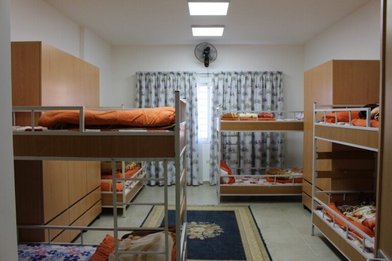 غرفة تحتوي أسرّة طابقية مرتبة داخل سكن طلابي في مبرة الإمام الرضا (ع) في لبنان | Room with arranged bunk beds inside a student dormitory at Imam Al-Ridha Institution in Lebanon