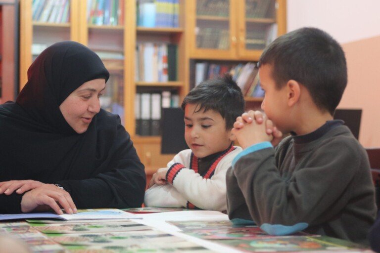 معلمة تعمل مع أطفال في نشاط تعليمي داخل مكتبة ضمن مبرة الإمام علي (ع) | Teacher working with children in an educational activity inside a library at Imam Ali Institution