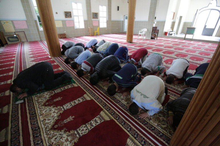 أطفال يؤدون الصلاة في قاعة صلاة داخل مبرة الإمام علي (ع) | Children performing prayer in a prayer hall at Imam Ali Institution