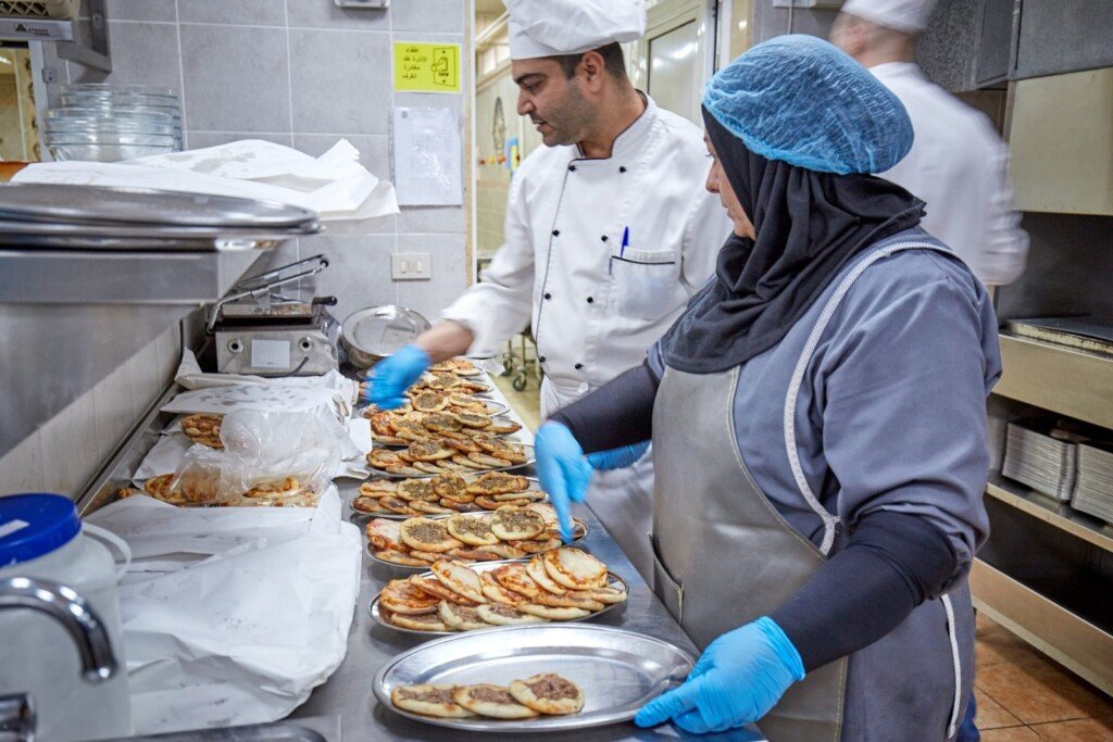 عاملان في المطبخ يقومان بتحضير وترتيب الطعام ضمن مبرة النبي إبراهيم (ع) في لبنان | Two staff members preparing and organizing food in a kitchen at Prophet Ibrahim Institution (AS) in Lebanon
