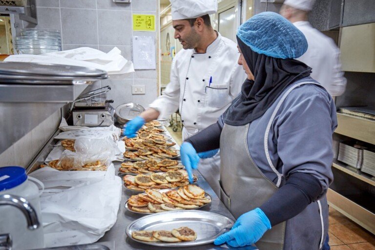 عاملان في المطبخ يقومان بتحضير وترتيب الطعام ضمن مبرة النبي إبراهيم (ع) في لبنان | Two staff members preparing and organizing food in a kitchen at Prophet Ibrahim Institution (AS) in Lebanon