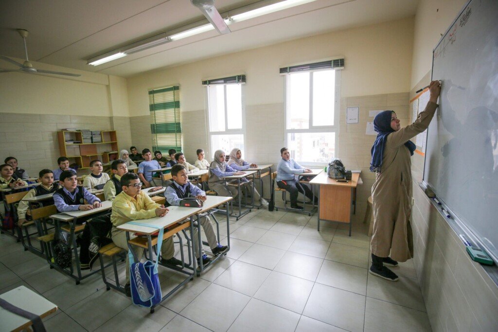معلمة تكتب على اللوح أمام طلاب في صف مدرسة الإشراق | A teacher writing on the board before students in a classroom at Al-Ishraq School