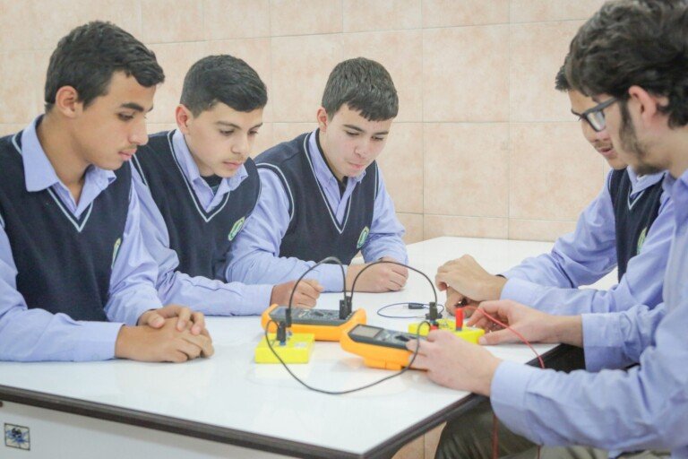 طلاب يجرون تجربة كهرباء بجهاز قياس رقمي في مختبر مدرسة الإشراق | Students conducting an electricity experiment with a digital multimeter in the lab of Al-Ishraq School