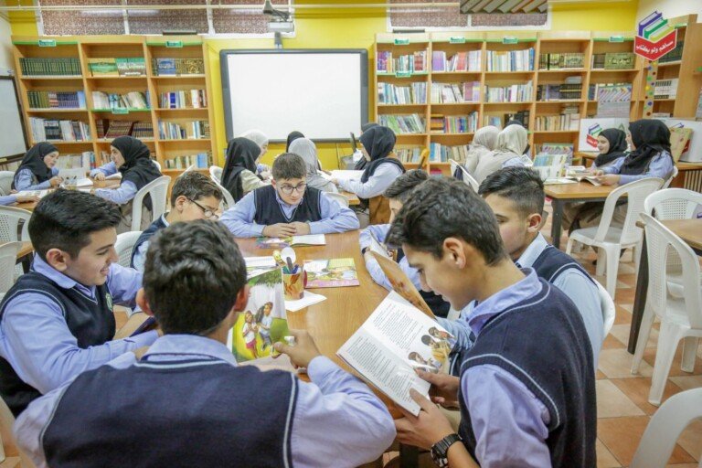 طلاب يقرؤون الكتب حول طاولات في مكتبة مدرسة الإشراق | Students reading books around tables in the library of Al-Ishraq School