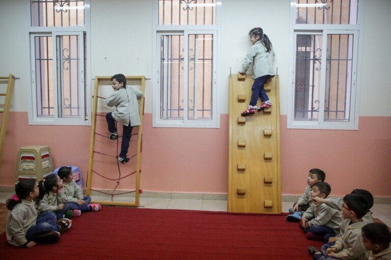 أطفال روضة يتسلقون سلماً خشبياً ومنحدراً في نشاط حركي بمدرسة الإشراق | Kindergarteners climbing a wooden ladder and ramp in a motor activity at Al-Ishraq School