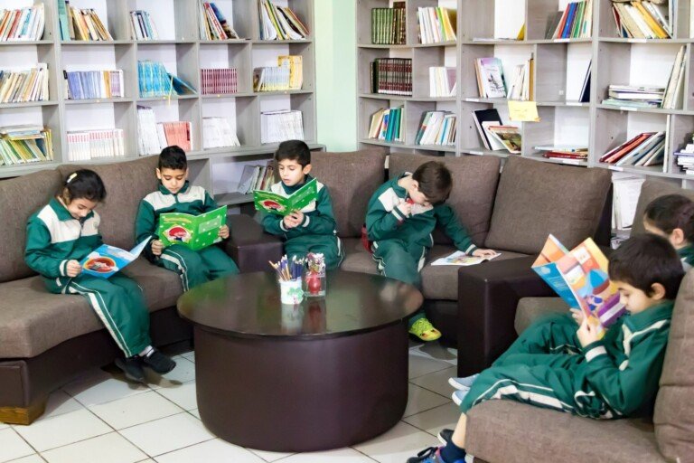 طلاب يقرؤون كتباً في ركن الجلوس داخل مكتبة مدرسية هادئة | Students reading books in a seating area inside a quiet school library