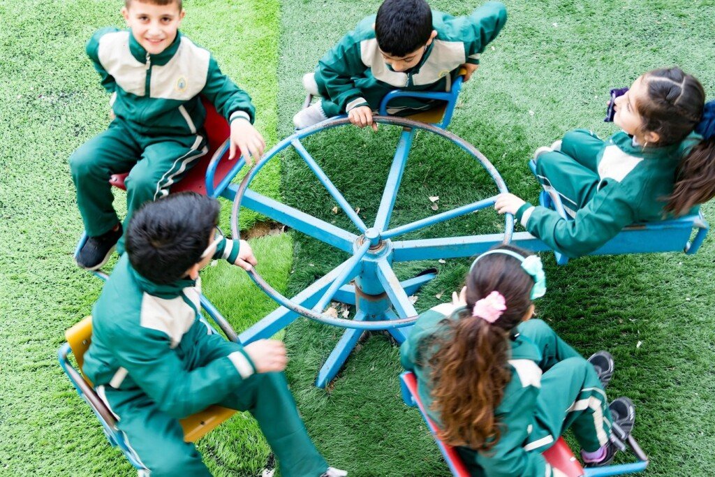طلاب يشاركون في نشاط لعب جماعي على جهاز دوّار في ساحة المدرسة | Students participating in a group play activity on a merry-go-round in a school playground