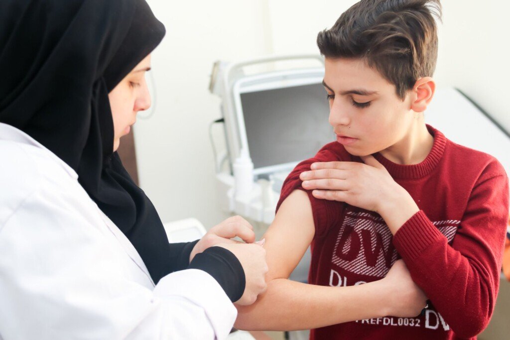ممرضة تعطي لقاحاً في ذراع فتى في مركز المصطفى الصحي | A nurse giving a boy a vaccine in his arm at Al-Mustafa Health Center