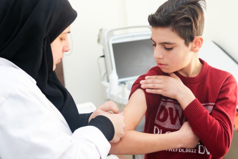 ممرضة تعطي لقاحاً في ذراع فتى في مركز المصطفى الصحي | A nurse giving a boy a vaccine in his arm at Al-Mustafa Health Center