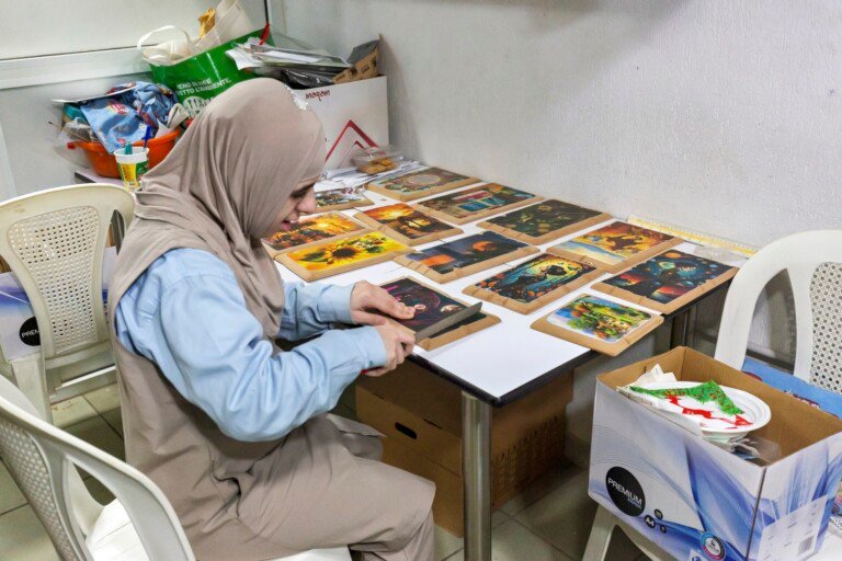 طالبة ترتّب لوحات فنية مطبوعة على طاولة في مؤسسة الإمام الهادي | A student arranging printed art cards on a table at Al-Imam Al-Hadi Institution