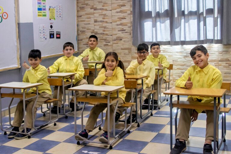 تلامذة بقمصان صفراء يرفعون إبهامهم بابتسامة في صف مؤسسة الإمام الهادي | Pupils in yellow shirts giving smiling thumbs-up in a classroom at Al-Imam Al-Hadi Institution