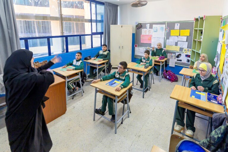معلمة تشرح بلغة الإشارة لطلاب بالزي الأخضر في صف مؤسسة الإمام الهادي | A teacher signing to students in green uniforms in a classroom at Al-Imam Al-Hadi Institution