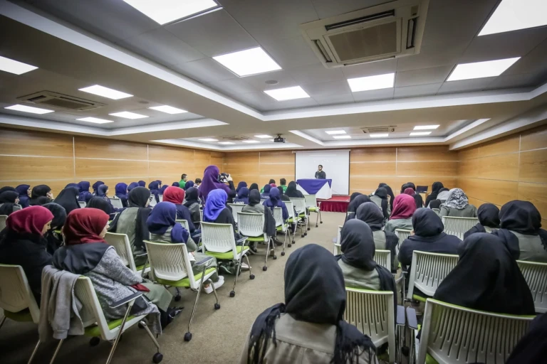 طالبات محجبات يستمعن إلى متحدث في قاعة محاضرات بدار الصادق للتربية والتعليم | Students in hijab listening to a speaker in a lecture hall at Dar Al-Sadiq for Education