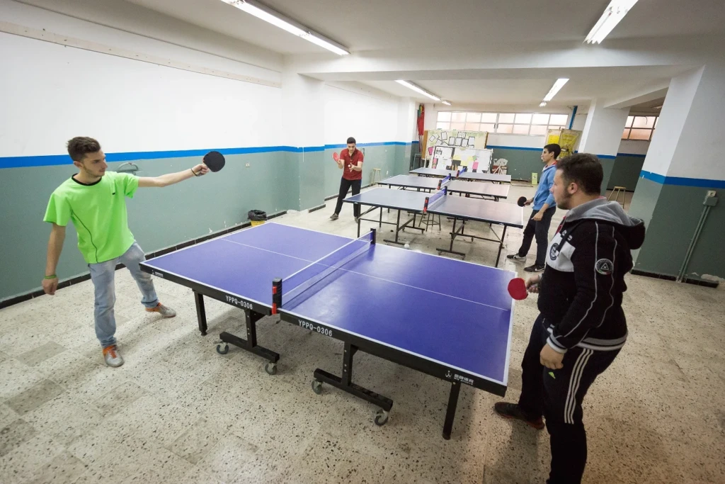 طلاب يلعبون كرة الطاولة في قاعة معهد علي الأكبر المهني والتقني | Students playing table tennis in a hall at Ali Al-Akbar Vocational and Technical Institute