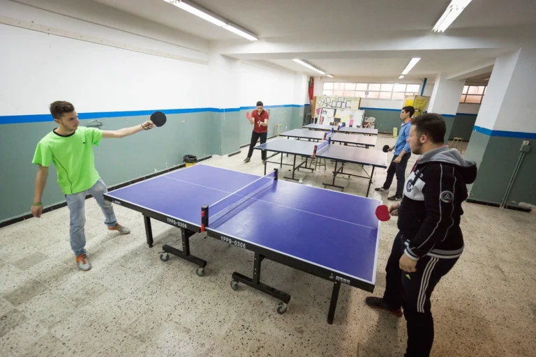 طلاب يلعبون كرة الطاولة في قاعة معهد علي الأكبر المهني والتقني | Students playing table tennis in a hall at Ali Al-Akbar Vocational and Technical Institute