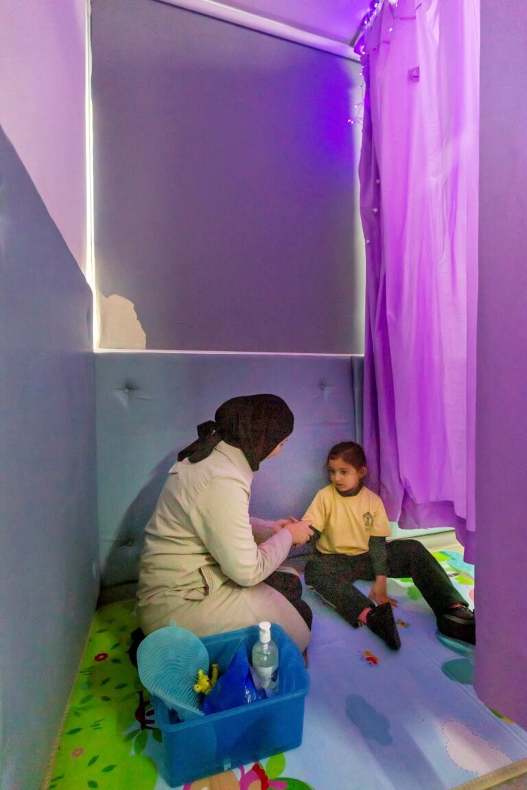اختصاصية مع طفلة في الغرفة الحسية بإضاءة بنفسجية في مركز الهادي HDIC | A specialist with a girl in the purple-lit sensory room at Al-Hadi Diagnostic Center HDIC