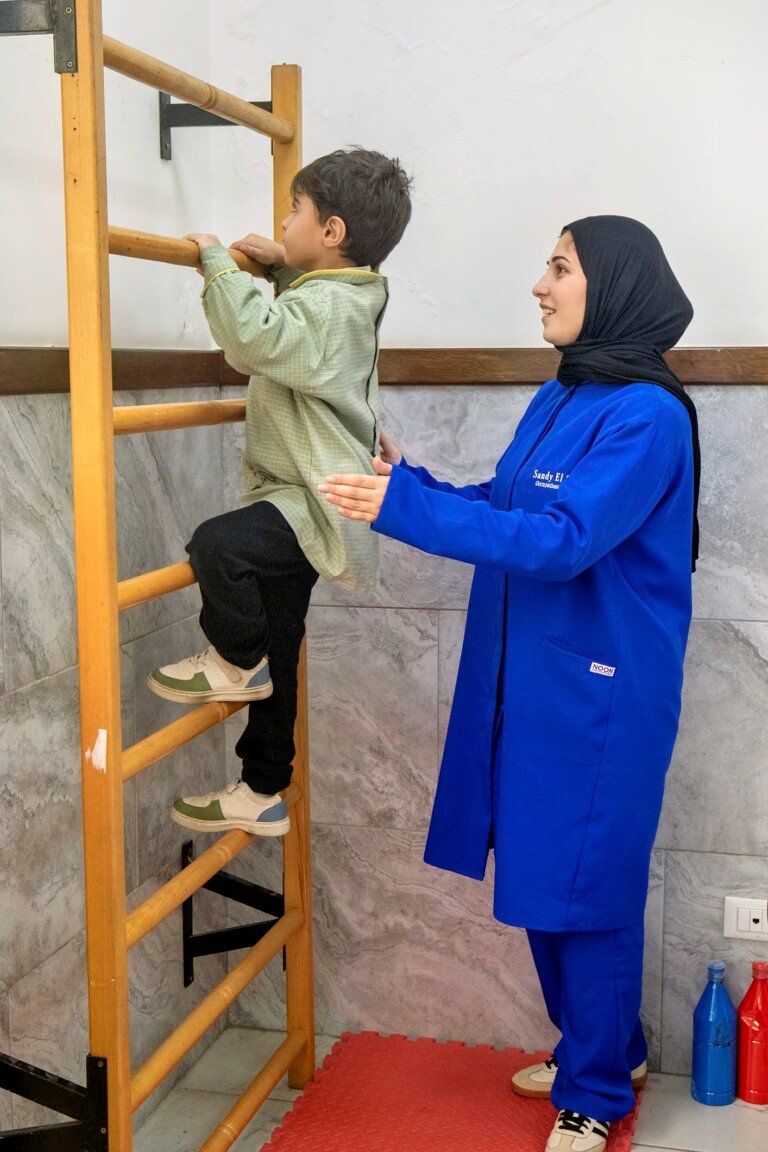 طفل يتسلق سلماً خشبياً بإشراف معالجة وظيفية في مركز سراج | A child climbing a wall-mounted wooden ladder supervised by an occupational therapist at Siraj Center
