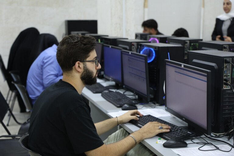طالب في جامعة USAL يعمل على الحاسوب في مختبر يضم صفوف أجهزة | A USAL university student working on a computer in a lab lined with rows of machines