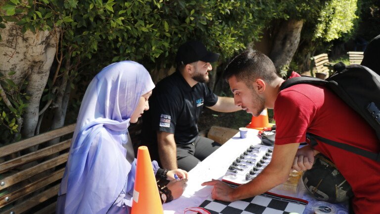 طالبان يتقابلان حول رقعة شطرنج في نشاط خارجي بجامعة USAL | Two students facing off over a chessboard at a USAL outdoor activity