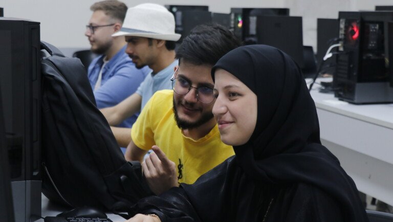 طلاب جامعة USAL يعملون معاً أمام شاشات الحاسوب في مختبر المعلوماتية | USAL university students working together at computer screens in the IT lab
